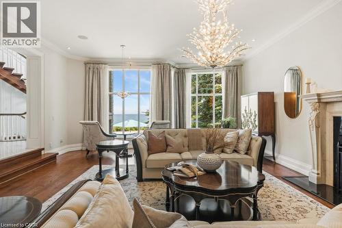 Hardwood flooring, ornate fireplace with stone mantel, large picture windows, decorative ceiling light fixture, and wood staircase - 4038 Lakeshore Road, Burlington, ON 