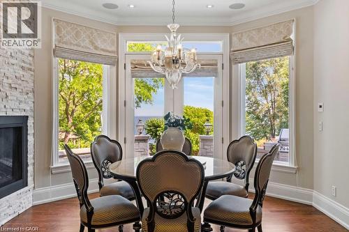 Bay window with multiple glass doors, stacked stone fireplace, wood-finish flooring, and crown molding - 4038 Lakeshore Road, Burlington, ON 