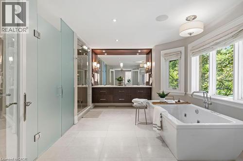 Freestanding soaking tub with polished chrome fixtures, dual vanity with wood-finish cabinetry, built-in mirror with sconce lighting, and frosted glass shower enclosure - 4038 Lakeshore Road, Burlington, ON 