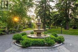 Circular paver driveway featuring a multi-tiered water fountain, surrounded by manicured shrubs - 