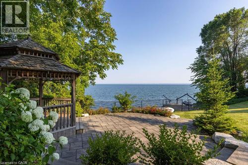 Waterside setting featuring a wooden gazebo with a shingled roof, a stone paver patio, mature trees, and a manicured lawn - 4038 Lakeshore Road, Burlington, ON 