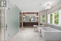 Freestanding soaking tub with polished chrome fixtures, dual vanity with wood-finish cabinetry, built-in mirror with sconce lighting, and frosted glass shower enclosure - 