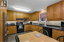 Kitchen featuring wood cabinetry, dark countertops, a tile backsplash, and stainless steel appliances - 