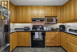 U-shaped kitchen featuring wood cabinetry, black countertops, a tile backsplash, and stainless steel appliances - 