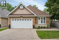 Brick and stone facade with a gable roof, featuring a paneled garage door with upper window inserts, a paver driveway, and a front window with white shutters - 