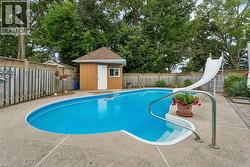 Inviting inground swimming pool with a white slide, surrounding concrete patio, and a dedicated storage shed - 