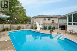 In-ground swimming pool with integrated steps, surrounded by a concrete patio, wood fencing, and mature trees - 