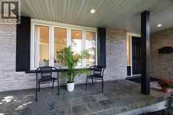 Front porch featuring slate tile flooring, stone veneer siding, white-framed windows with black shutters, and a black paneled entry door - 