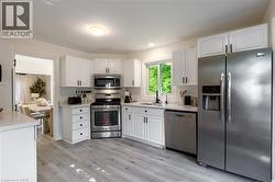 White cabinetry, stainless steel appliances, wood-finish flooring, white countertops, and a window above the sink - 