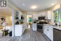 White cabinetry with black hardware, stainless steel appliances, light-toned countertops, subway tile backsplash, and wood-finish flooring - 