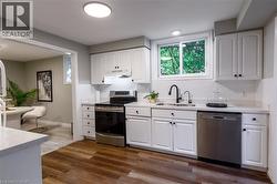 Kitchen featuring wood-finish flooring, white cabinetry, a stainless steel dishwasher, a stainless steel range, and a single-basin sink with a matte black faucet - 