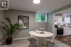 Wood-finish flooring throughout, with a window providing natural illumination, and a kitchen featuring white cabinetry, a black appliance suite, and a stainless steel sink - 