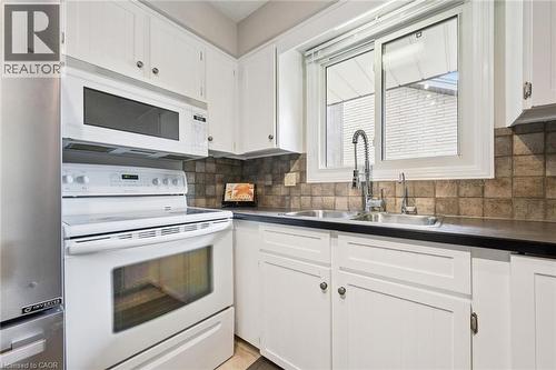 White cabinetry with dark hardware, stainless steel double basin sink, pull-down faucet, tile backsplash, and a large window - 21 Colebrook Court, Kitchener, ON 