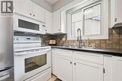 White cabinetry with dark hardware, stainless steel double basin sink, pull-down faucet, tile backsplash, and a large window - 