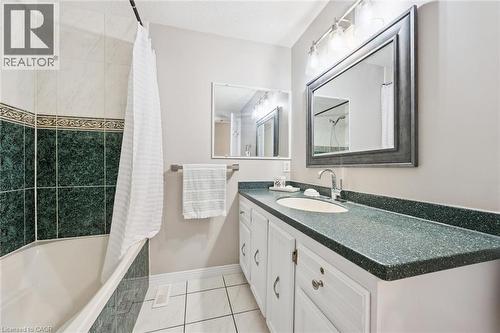 Bathroom featuring a white bathtub with green-tiled surround, white vanity with integrated sink, speckled countertop, and a framed mirror - 21 Colebrook Court, Kitchener, ON 