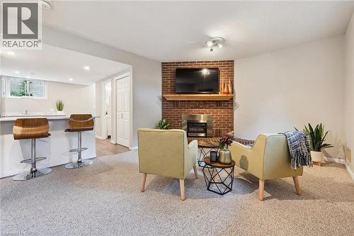 Carpeted living area featuring a brick fireplace with a wood mantel, an integrated bar with a solid surface countertop, recessed lighting, and a white paneled door - 21 Colebrook Court, Kitchener, ON 