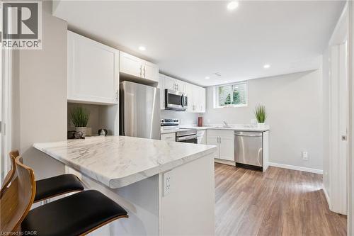 Kitchen featuring white cabinetry, stainless steel appliances, a breakfast bar with a stone-finish countertop, and wood-finish flooring - 21 Colebrook Court, Kitchener, ON 