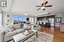 Open-concept living area with wood-finish flooring, a tray ceiling, and expansive windows - 