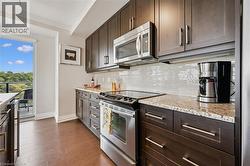 Kitchen featuring wood-finish flooring, dark wood cabinetry with stainless steel hardware, a white tile backsplash, and light-toned countertops - 