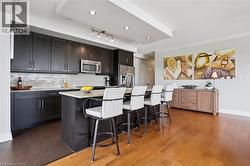 Kitchen featuring dark wood-finish cabinetry, stainless steel appliances, a tile backsplash, and an island with counter seating - 