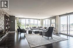 Expansive living area featuring wide plank wood-finish flooring, a built-in stone accent wall with integrated shelving, recessed lighting, and multiple arched windows - 