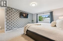 Textured accent wall, ceiling-mounted light fixture, light-toned carpeting, and a window with exterior views - 