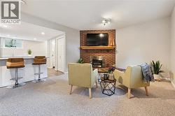 Carpeted living area featuring a brick fireplace with a wood mantel, an integrated bar with a solid surface countertop, recessed lighting, and a white paneled door - 