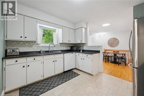 Kitchen featuring white cabinetry, dark countertops, a tile backsplash, and a built-in dishwasher - 135 Bridge Street W, Waterloo, ON 