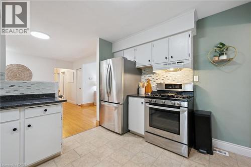 Kitchen featuring stainless steel appliances, white cabinetry with dark hardware, dark countertops, and a mosaic tile backsplash - 135 Bridge Street W, Waterloo, ON 