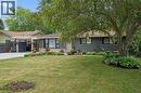 Front exterior featuring a brick facade with stone detailing, a covered carport, mature trees, manicured landscaping, and a paved driveway - 135 Bridge Street W, Waterloo, ON 