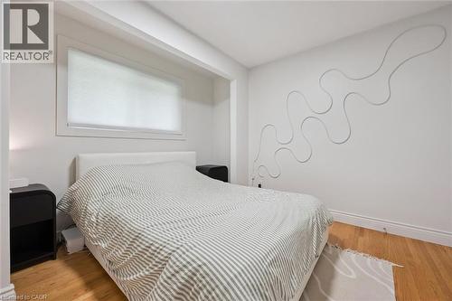 Bedroom featuring wood-finish flooring, a contemporary wall accent, and a window with a cellular shade - 135 Bridge Street W, Waterloo, ON 