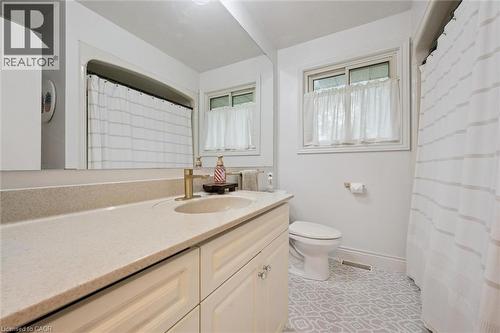 Full bathroom featuring a single vanity with an integrated sink, a large wall mirror, a window with trim, and patterned floor tile - 135 Bridge Street W, Waterloo, ON 