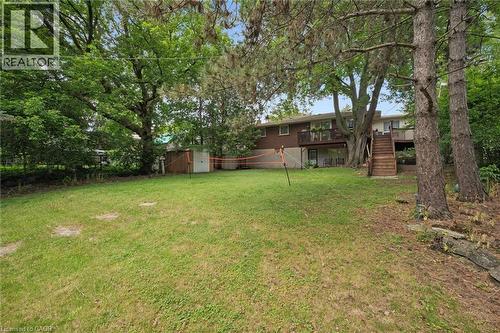 Expansive backyard featuring a large grass area, mature trees, a detached storage shed, a two-story residence with a lower-level walkout, and an upper-level balcony accessible by exterior wood stairs - 135 Bridge Street W, Waterloo, ON 