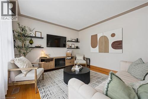 Living area featuring hardwood flooring, a patterned area rug, a built-in media console with fireplace, a wall-mounted television, and floating wall shelves - 135 Bridge Street W, Waterloo, ON 