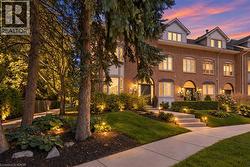Brick facade with multiple dormer windows, featuring a multi-level concrete walkway, landscaped grounds, and integrated exterior lighting - 