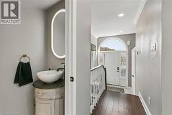 Custom vanity with vessel sink, illuminated oval mirror, dark wood-finish flooring, recessed lighting, and arched entry door with side lites - 