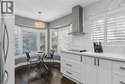 Bay window with custom plantation shutters, wood-finish flooring, white cabinetry with matte black hardware, stainless steel range hood, and white veined backsplash - 
