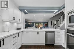 White cabinetry with black hardware, integrated stainless steel appliances, wood-finish flooring, white countertop, and a contemporary linear ceiling light fixture - 