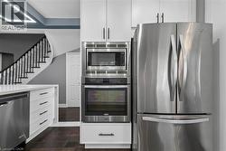 Integrated stainless steel appliances, white cabinetry with dark hardware, dark wood-finish flooring, and a curved staircase with white balusters - 