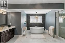 Freestanding soaking tub with a decorative pendant light, a large vanity with white countertop, and a glass-enclosed shower - 