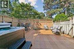 Expansive outdoor patio featuring a hot tub, wood-finish decking, and slatted privacy fencing - 