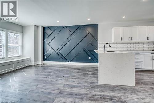 Engineered wood-finish flooring, recessed lighting, accent wall with geometric paneling, white kitchen cabinetry with black hardware, and an island with an undermount sink - 23 Gibson Avenue, Hamilton, ON 