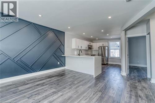 Open-concept living space with wood-finish flooring, a decorative accent wall, recessed lighting, and a kitchen featuring white cabinetry, a subway tile backsplash, and stainless steel appliances - 23 Gibson Avenue, Hamilton, ON 