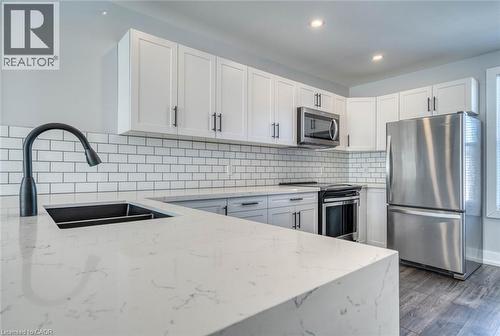 White shaker-style cabinetry, stainless steel appliances, white subway tile backsplash, and wood-finish flooring - 23 Gibson Avenue, Hamilton, ON 