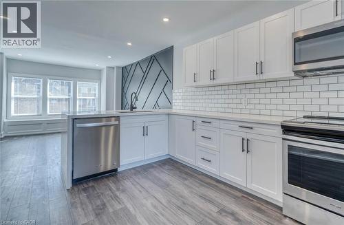 Contemporary kitchen featuring white cabinetry, subway tile backsplash, stainless steel appliances, and wood-finish flooring - 23 Gibson Avenue, Hamilton, ON 