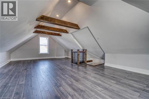 Spacious attic room featuring wood-finish flooring, exposed ceiling beams, recessed lighting, and a single window - 23 Gibson Avenue, Hamilton, ON 