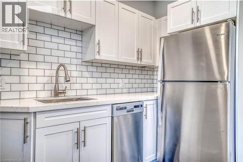 Kitchen featuring white cabinetry, white subway tile backsplash, stainless steel appliances, and a stainless steel sink with a gooseneck faucet - 23 Gibson Avenue, Hamilton, ON 