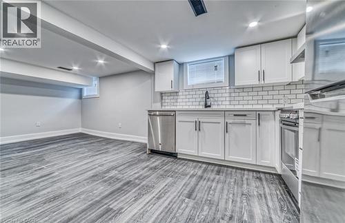Kitchenette featuring white shaker cabinetry, stainless steel appliances, subway tile backsplash, and wood-finish flooring - 23 Gibson Avenue, Hamilton, ON 