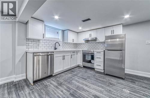 White cabinetry with matte black hardware, subway tile backsplash, stainless steel appliances, wood-finish flooring, and recessed ceiling lighting - 23 Gibson Avenue, Hamilton, ON 