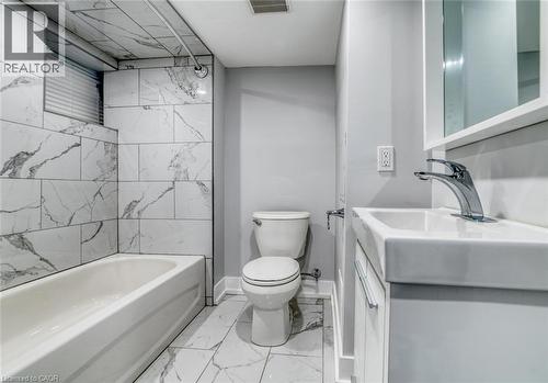 Bathroom featuring a bathtub with a shower, large format wall and floor tiling, a white vanity with an integrated sink, and a mirrored cabinet - 23 Gibson Avenue, Hamilton, ON 